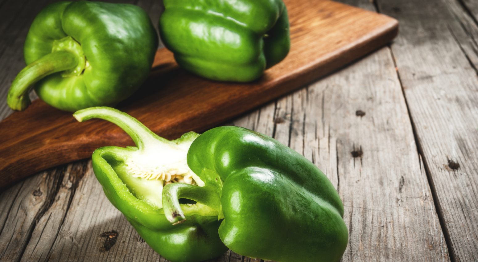 A green pepper being sliced on a cutting board