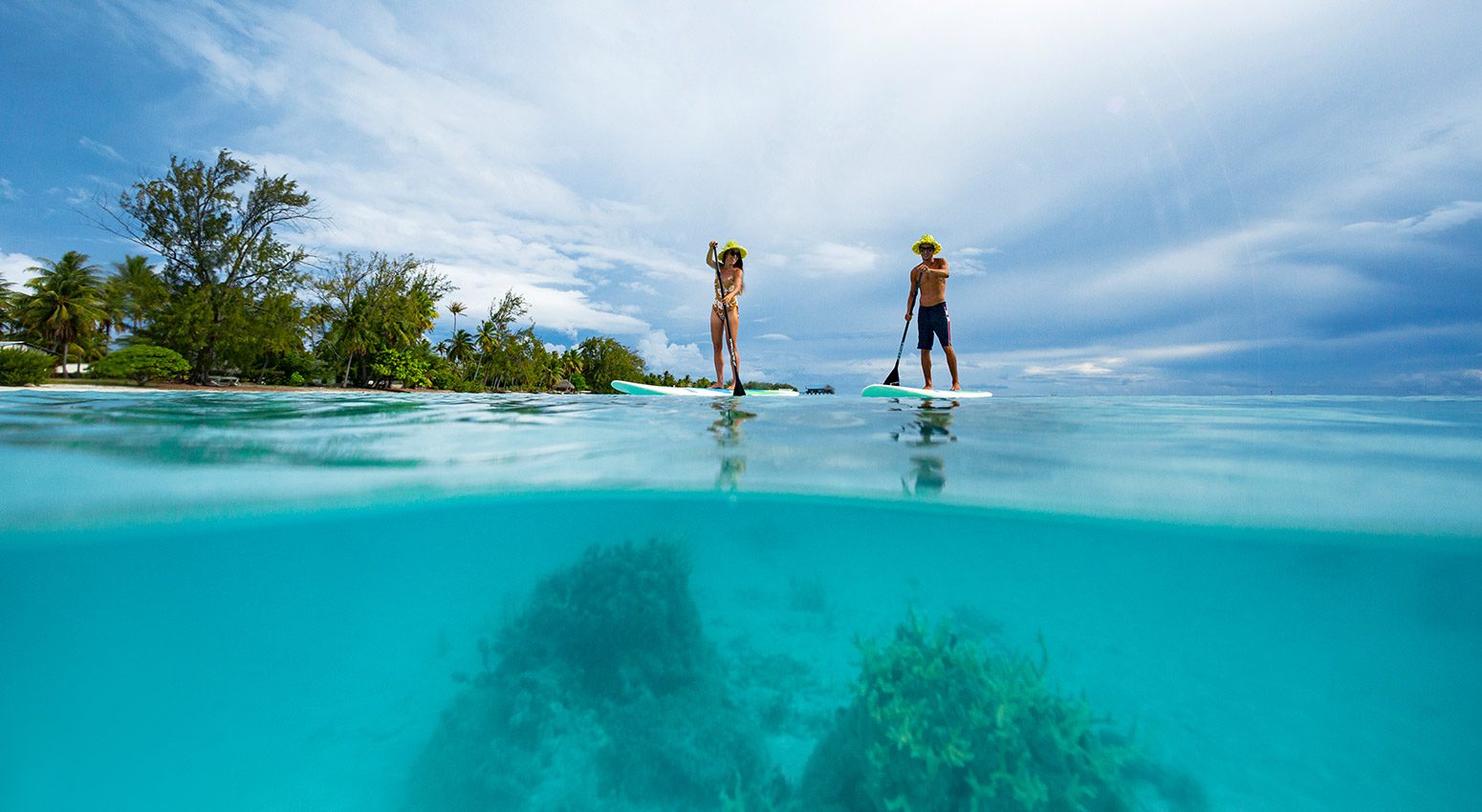 A man and a woman kayaking in turcquoise waters with a tropical island on the background