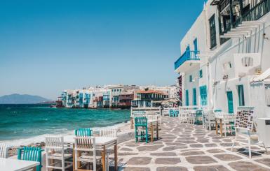 A view of Mykonos island from a cruise ship with clear blue water and white houses on the hills