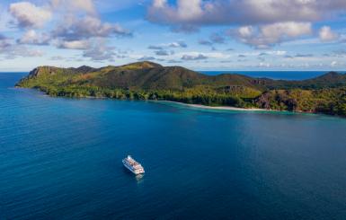 A bird's-eye view of a Variety Cruises ship sailing in the sea with a tropical island in the background