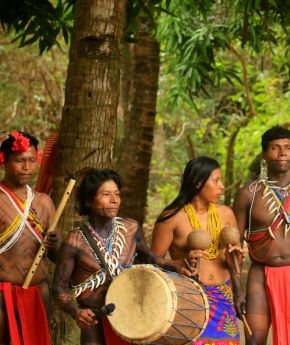 People in traditional clothing and face paint posing for a photo in front of a river and lush forest