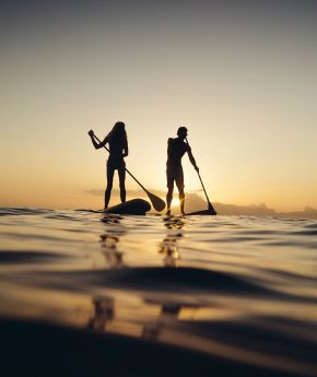 A man and a woman kayaking with the sunset on the background