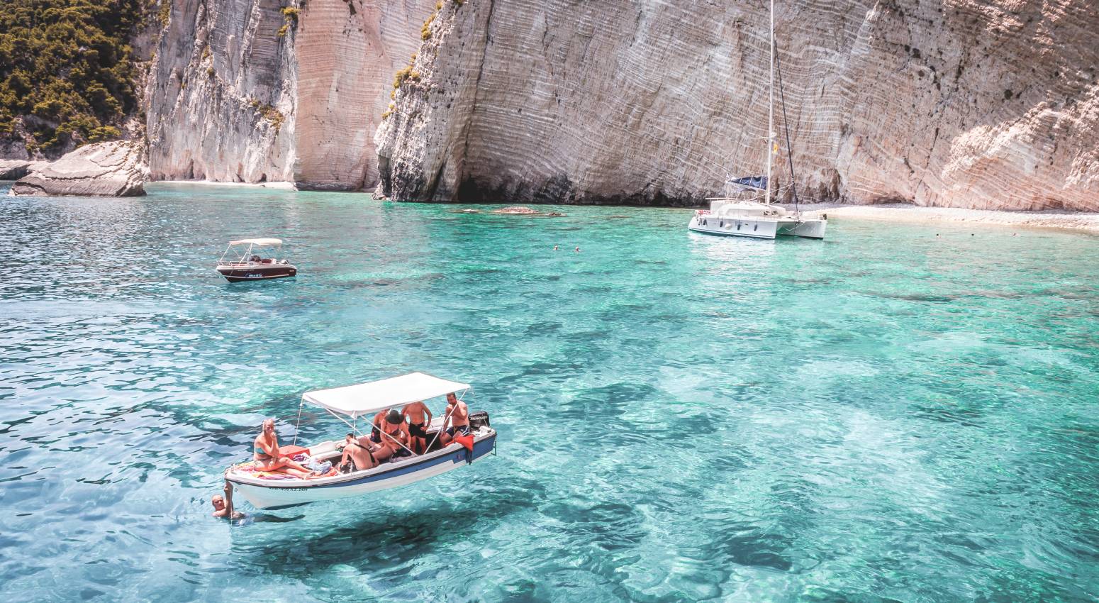 Small boats with tourists in turcquoise waters with a rocky beach in the background