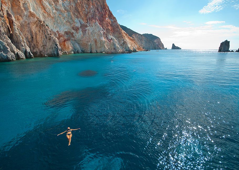 A woman swimming in the turquoise sea with rocky mountains in the background