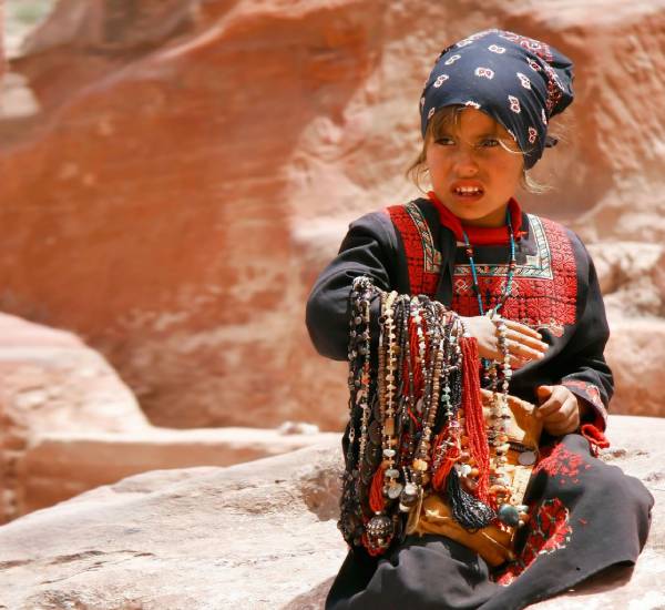 A child standing in front of the Petra Treasury with rock formations in the background