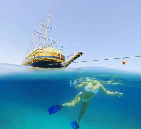 A woman snorkeling in the ocean with a Variety Cruises ship anchored in the background