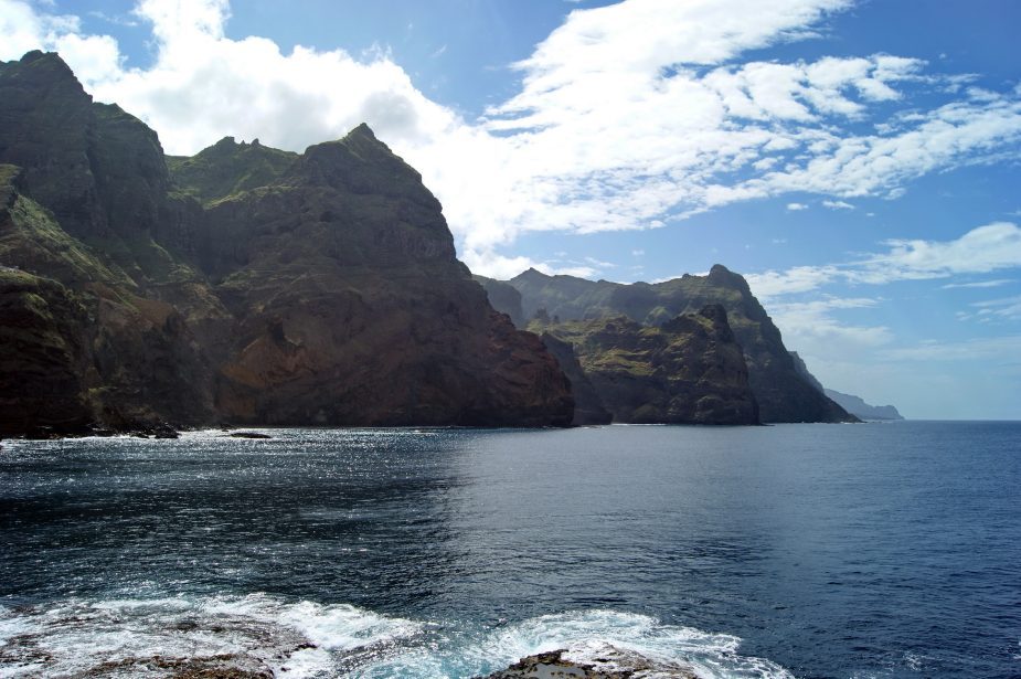 A lush green mountainous landscape with a blue ocean in the background