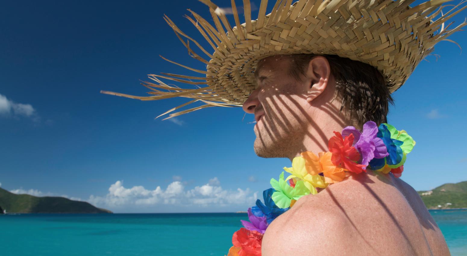 A man wearing a hat and a traditional necklace of colourful flowers with the sea in the background