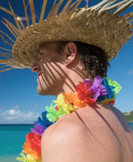A man wearing a hat and a traditional necklace of colourful flowers with the sea in the background
