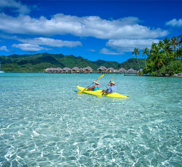 People kayaking in turquoise waters with a tropical island in the background