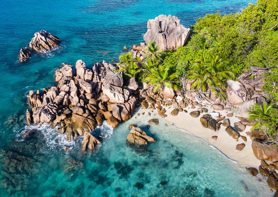 A tropical beach with turquoise waters and a rocky cliff in the background in the Seychelles Variety Cruises