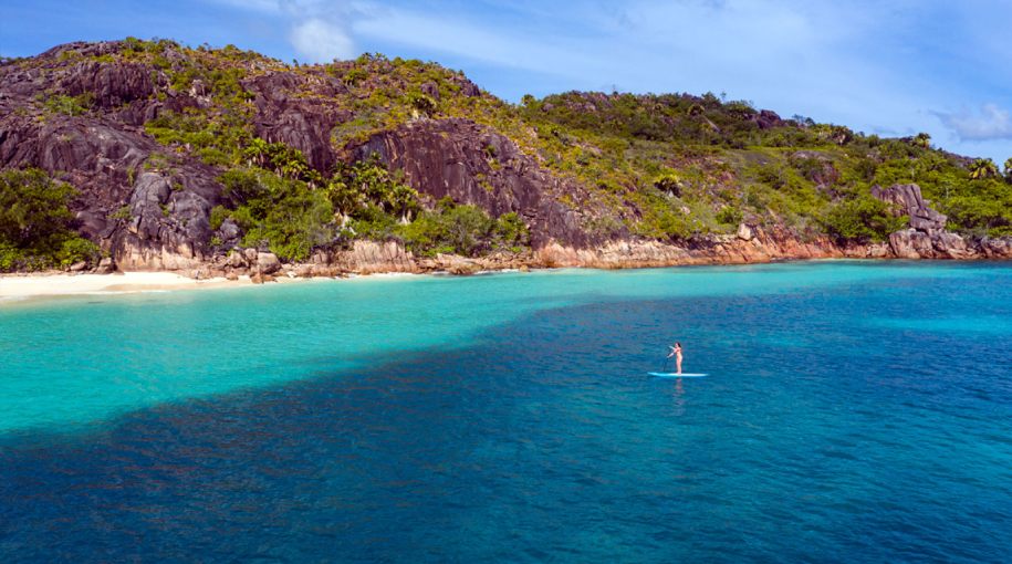 A person kayaking alone in calm, clear blue waters surrounded by lush greenery