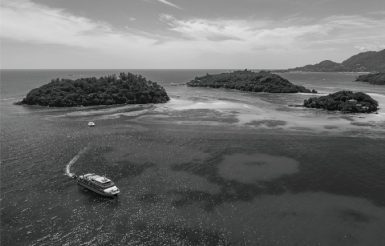 Black and white photo of a small ship in the sea with tropical islands in the background