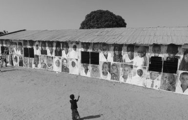 Black and white photo of an african kid staring a wall with children's photos