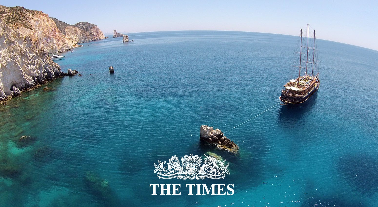 Variety Cruises named Best Cruise Line in the Times UK, a panoramic view to anchored Variety Cruises ship with rocky mountains in the background in Milos Island