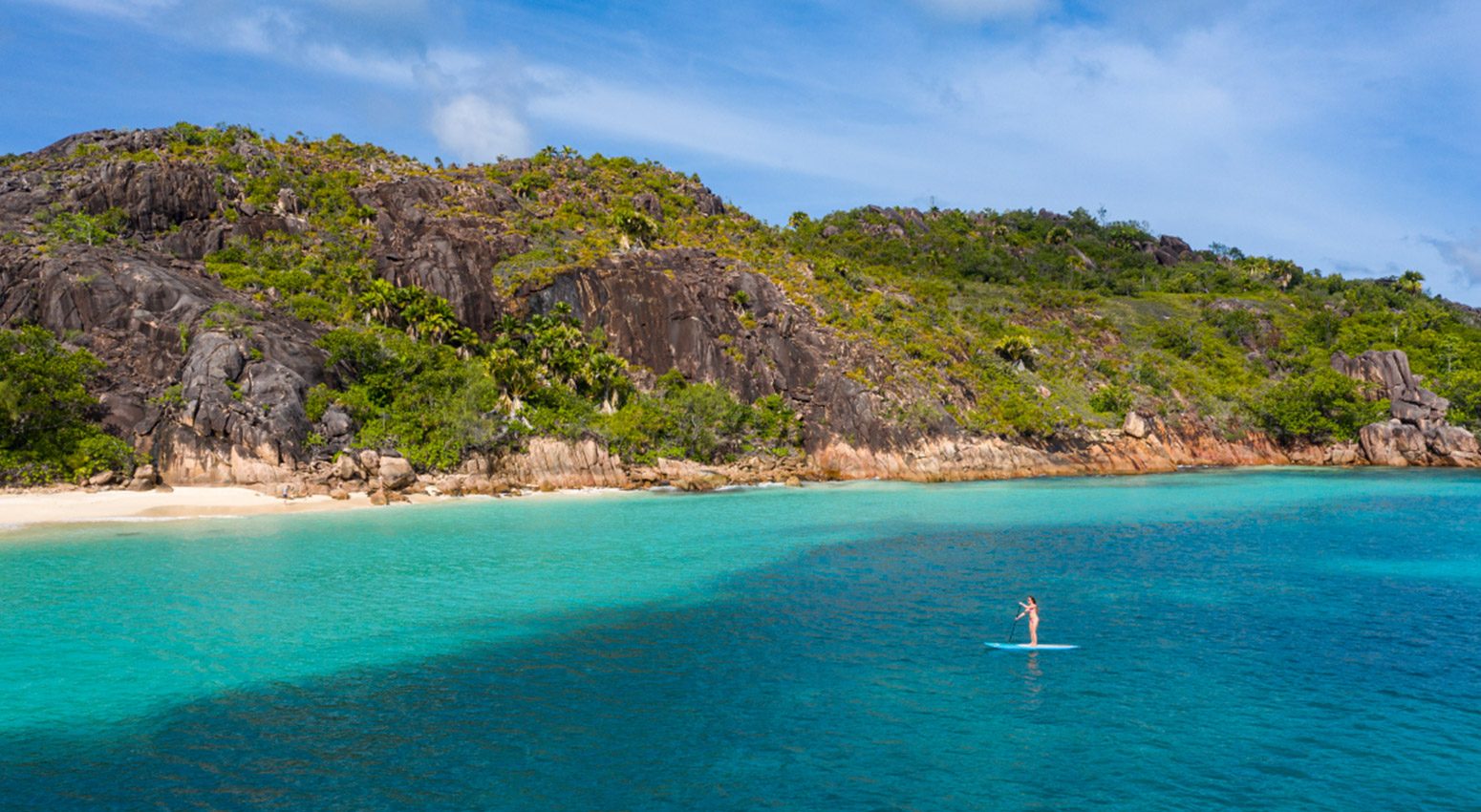 a woman kanoying in the sea with tropical island on the background