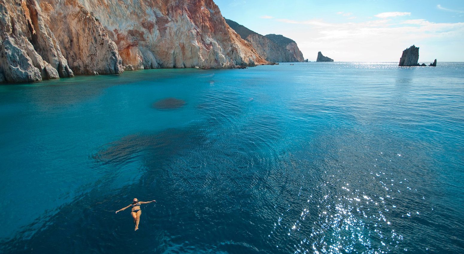 A woman swimming in the turquoise sea with rocky cliffs in the background