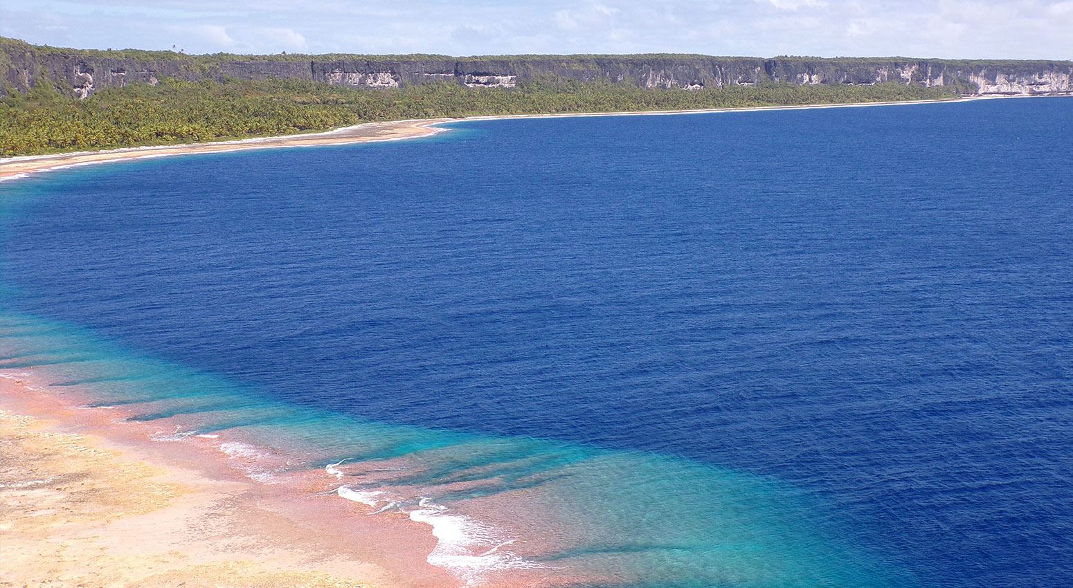 A beach and the deep blue see with green hills in the background.