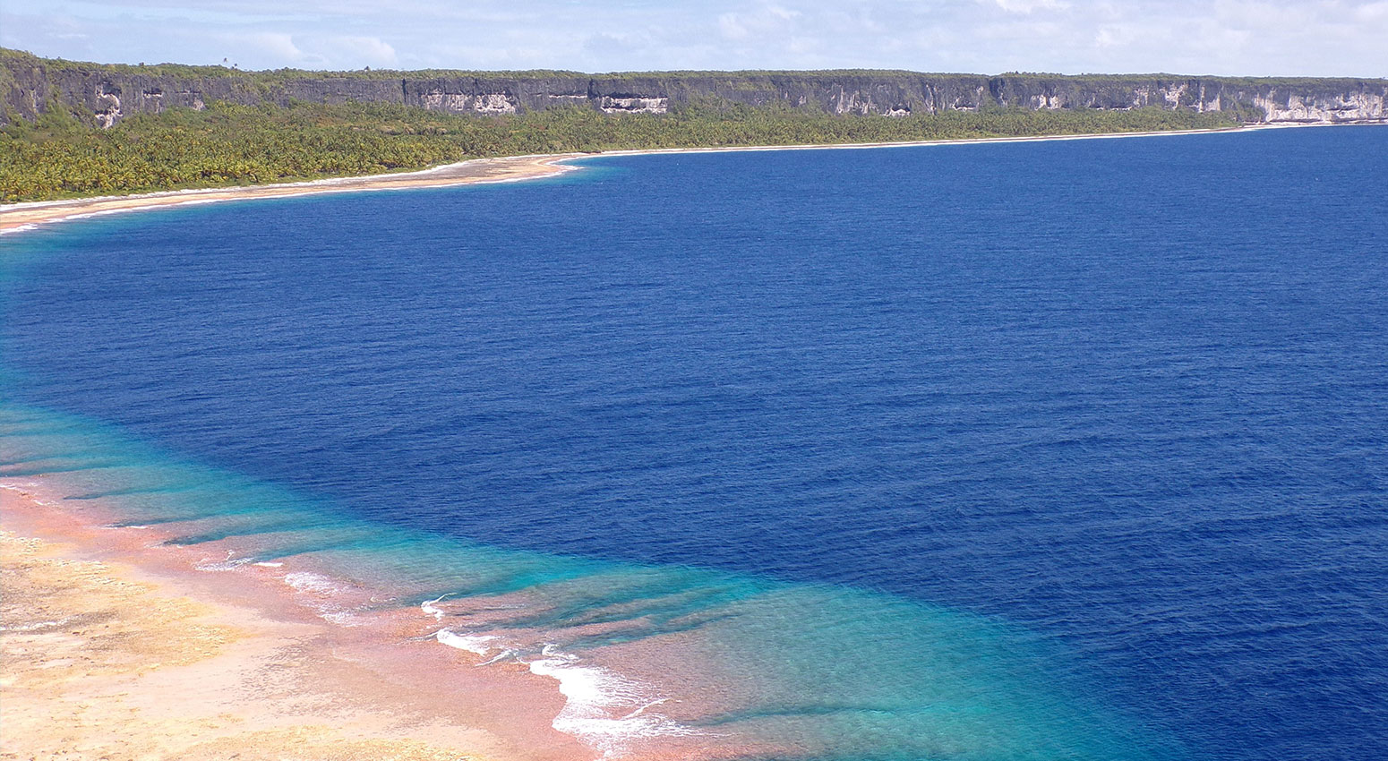 A beach and the deep blue see with green hills in the background.