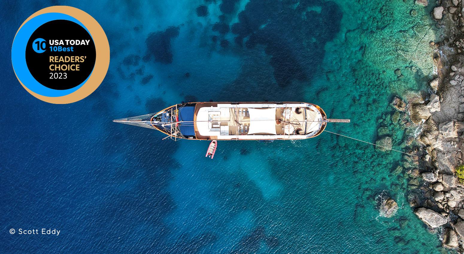 Aerial view of a ship anchored in turcquoise waters next to a rocky beach