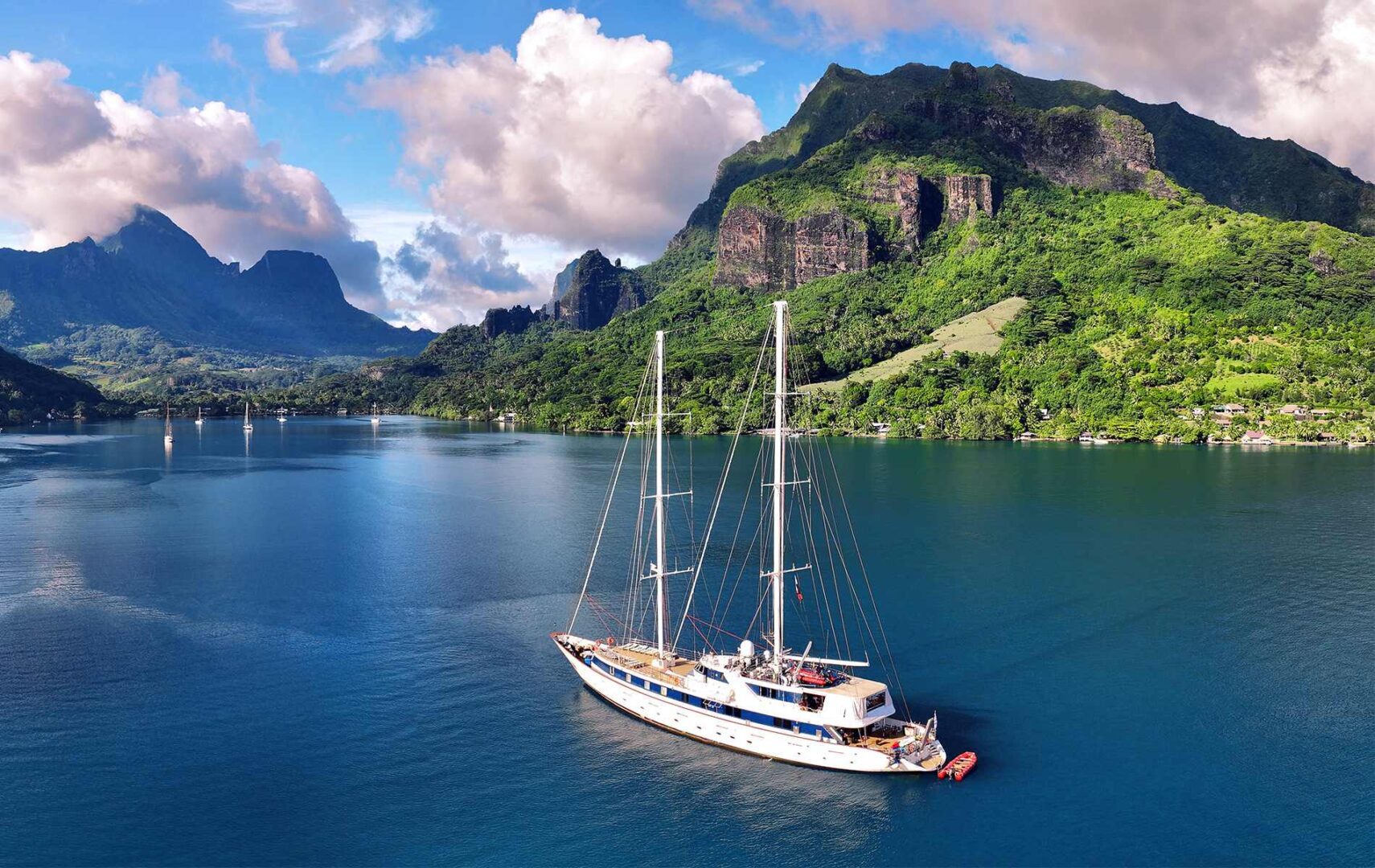 A large, three-masted sailing ship with white sails furled, floating on the calm blue waters of a bay